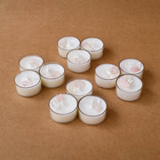 White tealight candles with quartz and rose stones on brown background